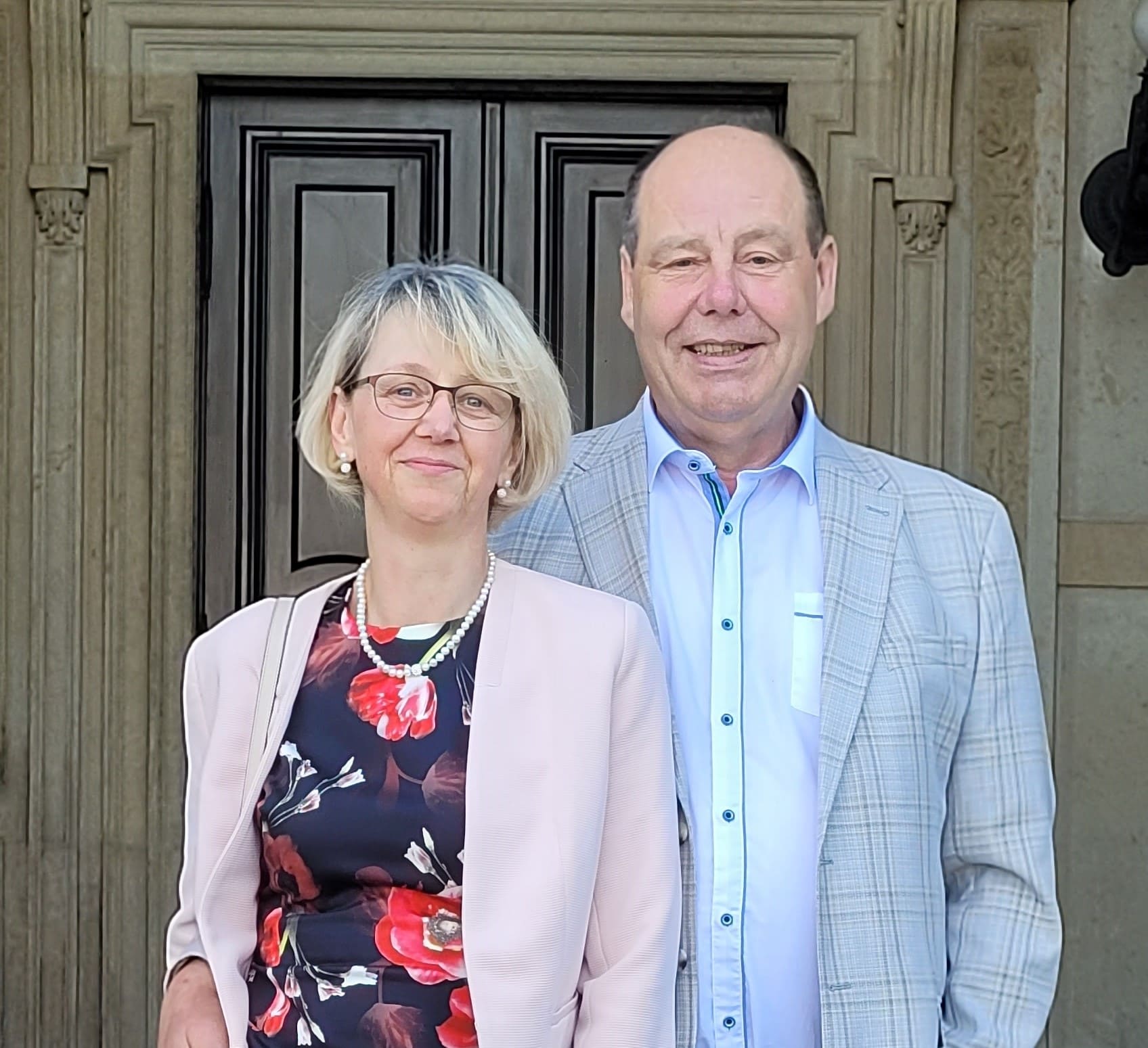 Janina und Heinz-Peter Fuhr, die Inhaber des Unternehmens, stehen gemeinsam vor einer historischen Tür. Beide lächeln herzlich in die Kamera und tragen elegante, festliche Kleidung. Die kunstvoll verzierte Tür im Hintergrund verleiht dem Bild eine besondere, traditionsbewusste Atmosphäre. Das Bild symbolisiert Vertrauen, Erfahrung und persönliche Nähe im Unternehmen